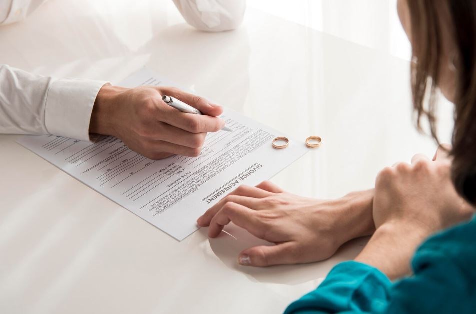 persona sentada a la mesa junto con su abogado, sobre la mesa documentación de divorcio y alianzas matrimoniales